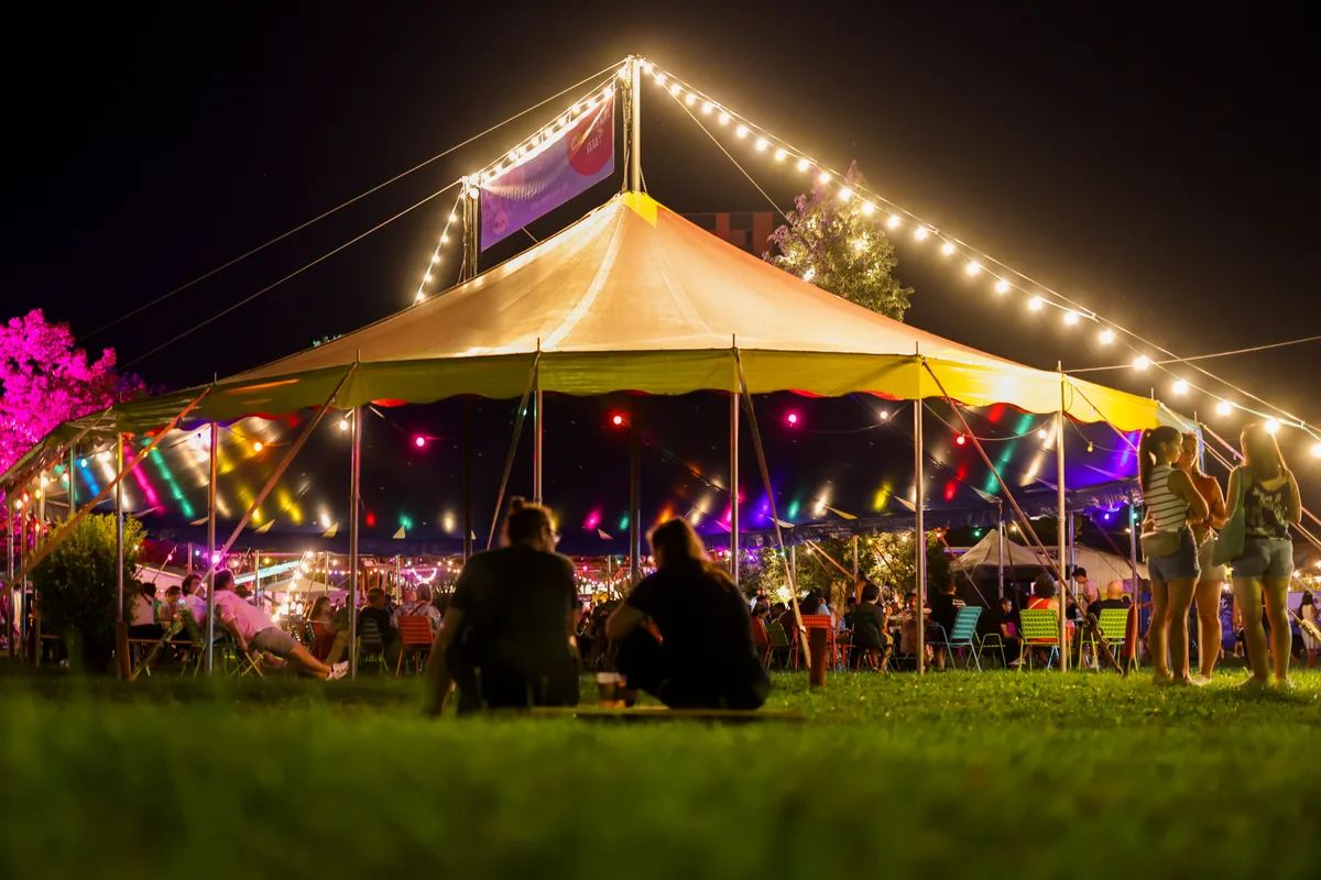 Einfach nur gemütlich: Sitzmöglichkeiten gibt es genug. Auf einer Wiese vor einem offenen Zelt sitzen zwei Menschen.